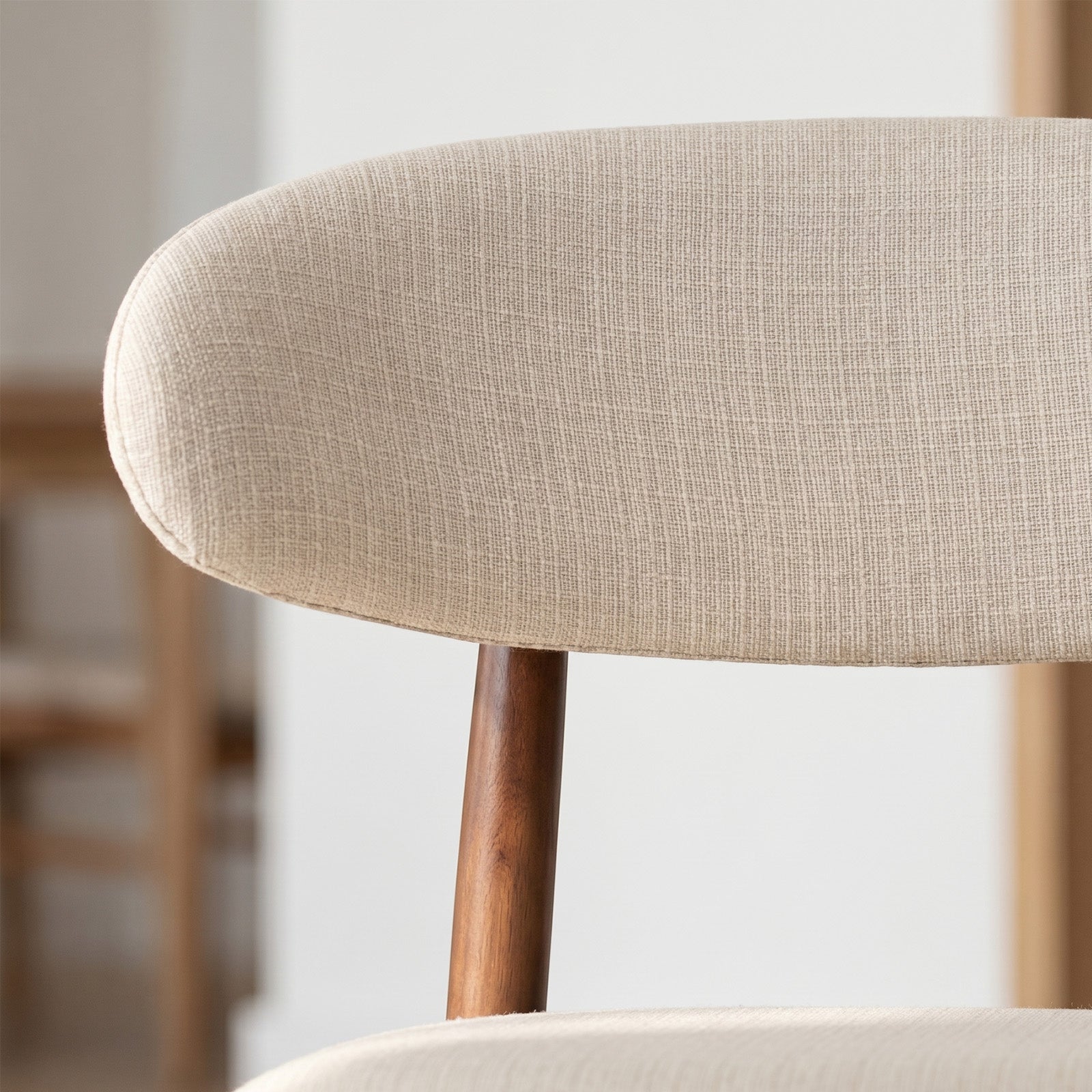 Close-up of a beige upholstered bar stool with wooden legs on a blurred background